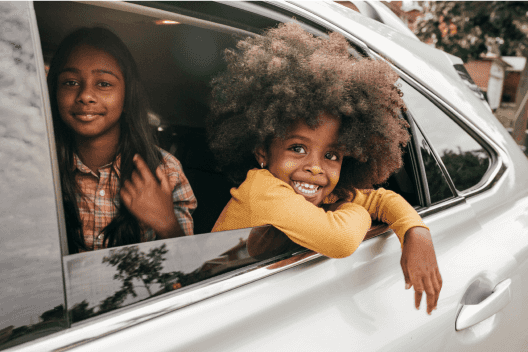 Two smiling kids sitting in a car with the window rolled down
